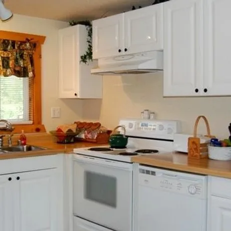 A kitchen with white cabinets, a stove, dishwasher, sink, and various items on the wooden countertops.