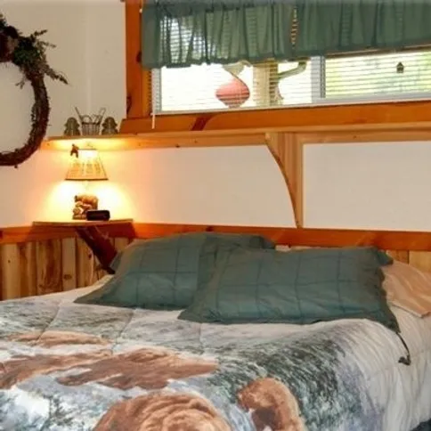 A cozy bedroom with a wooden headboard, two green pillows, a printed bedspread, and a lamp on a small shelf.
