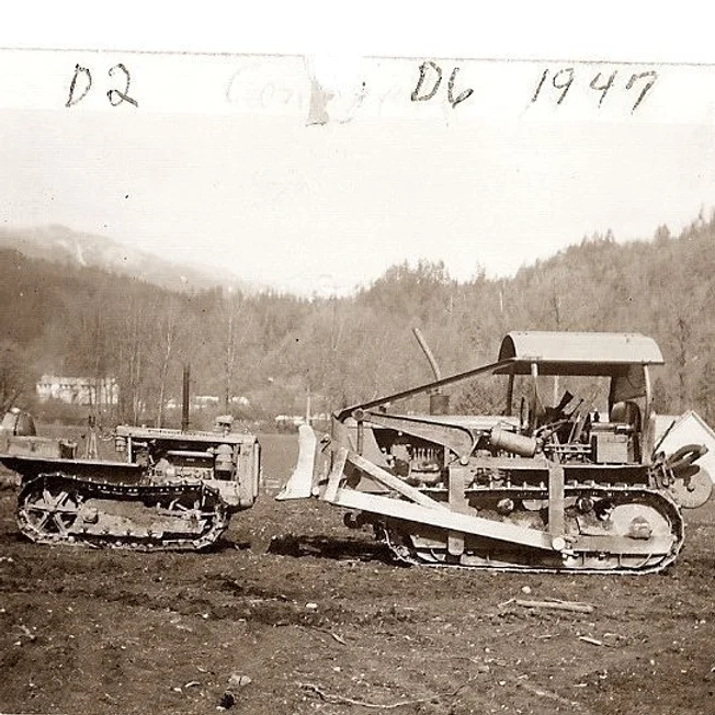 Two vintage Caterpillar bulldozers, a D2 and a D6, parked on dirt with trees and hills in the background, 1947.