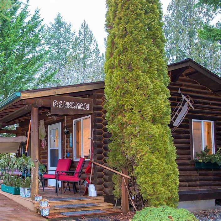 A log cabin labeled "Fisherman" with red chairs on the porch, surrounded by tall trees and greenery.